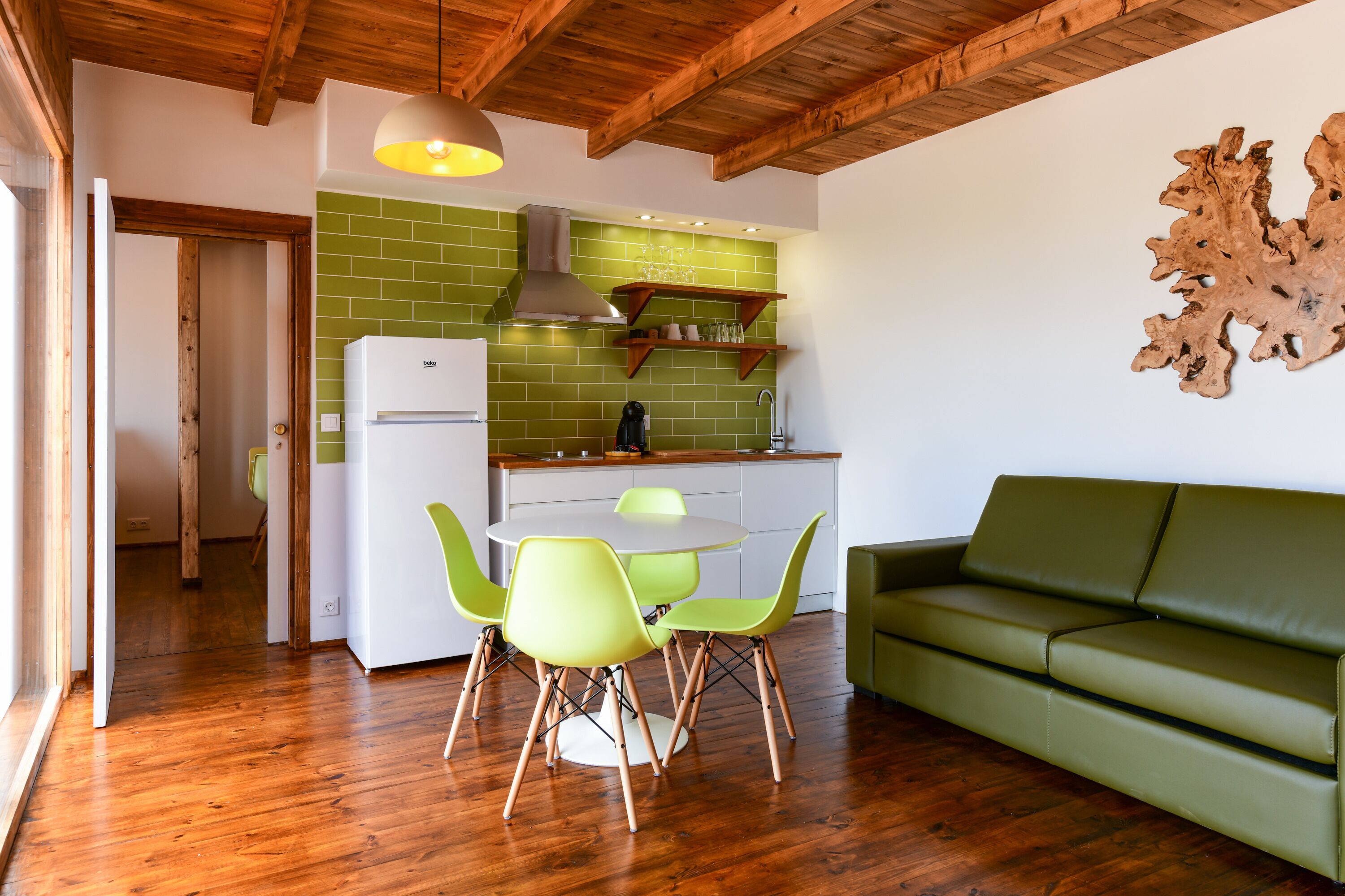 A modern kitchen with green tiles, a white refrigerator, and a dining area with a round table and green chairs.