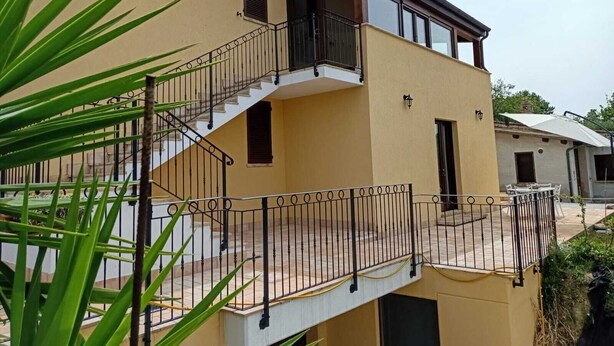 Un edificio de dos pisos con balcón, escalera y un pequeño espacio para sentarse al aire libre.