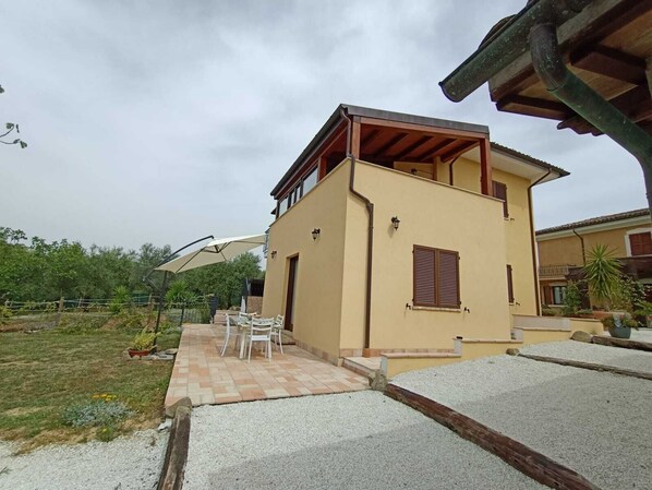 Ein zweistöckiges Haus mit einer Terrasse und Gartenmöbeln.
