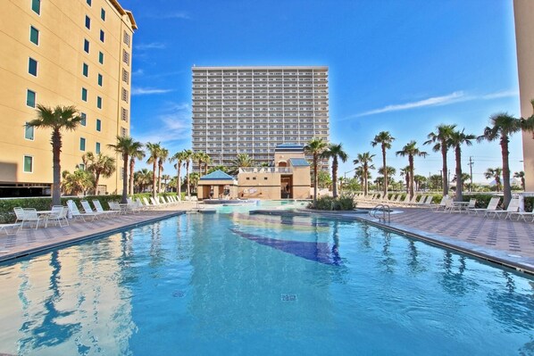 A swimming pool with lounge chairs and palm trees, surrounded by buildings. - Crystal Tower 1801 (Gulf Shores)