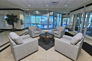 A lobby with two grey armchairs, a glass coffee table, and a large window overlooking a pool area. - Crystal Tower 1801 (Gulf Shores)