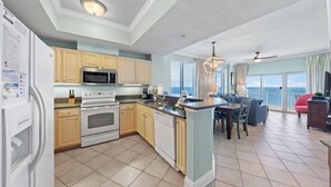 A modern kitchen with a central island, built-in appliances, and a dining area with a view. - Crystal Tower 1801 (Gulf Shores)