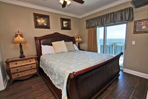 Ein Schlafzimmer mit einem großen Bett, zwei Nachttischen, einem Deckenventilator und Meerblick durch eine Schiebetür.
