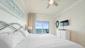 A bedroom with a large bed, a ceiling fan, a TV, and a window with a view. - Crystal Tower 1507 (Gulf Shores)