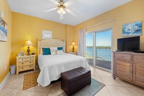 A bedroom with a bed, bedside tables, a TV, a balcony with a view, and a ceiling fan. - Crystal Tower 1809 (Gulf Shores)