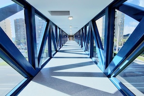 A covered pedestrian walkway with glass panels and metal beams, leading to a building entrance.