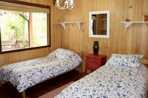 A room with two single beds, a wooden wall, a window, a mirror, and a red nightstand. - Great house with pool and native trees:  special for the solar eclipse (Pucón)