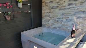 A spa tub with a stone wall backdrop, a potted plant, and a bottle of champagne on a tray. - Gite les marmottes with private spa (GERARDMER)