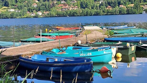 A calm lake with boats docked, surrounded by a forested hillside and a small village. - Gite les marmottes with private spa (GERARDMER)