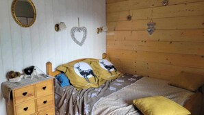 A bedroom with a wooden headboard, a bed with patterned bedding, a dresser with heart-shaped handles, a mirror, and wall decorations including a heart and animal motifs. - Gite les marmottes with private spa (GERARDMER)