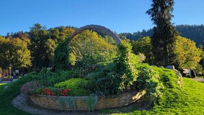 A garden with a circular stone structure surrounded by lush greenery and flowers. - Gite les marmottes with private spa (GERARDMER)
