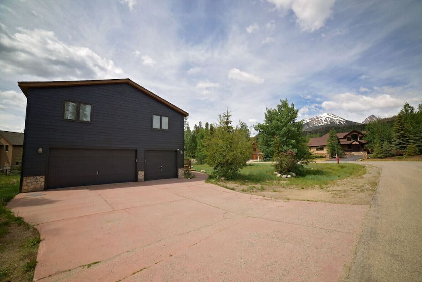 A two-story building with a dark exterior, a garage, and a driveway leading to a mountain backdrop.