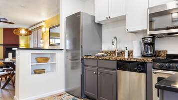 Una cocina moderna con un refrigerador de acero inoxidable, lavavajillas integrado, cafetera y microondas.