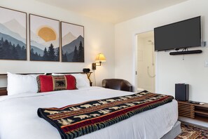 Ein Hotelzimmer mit einem großen Bett, einem wandmontierten Fernseher, einem Schreibtisch mit Computer und einem Duschbereich.