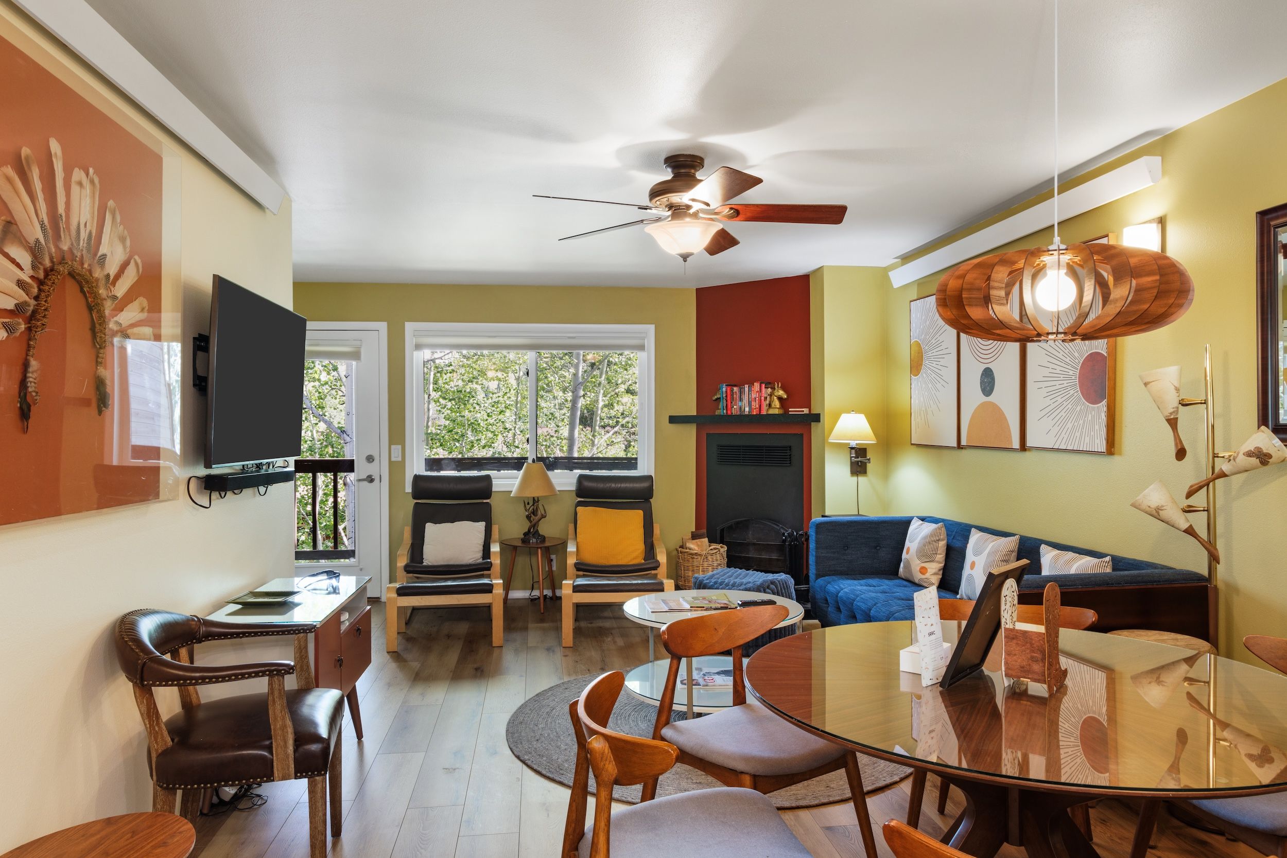 A modern living room with a ceiling fan, a fireplace, a blue sofa, and a dining table with chairs.