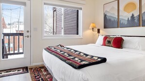 A bedroom with a bed, a window, a door, and a wall-mounted lamp. - Outpost: Pitchfork 452 - Close to Snow King Mtn! (Jackson)