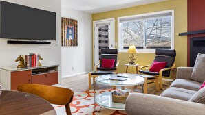 A living room with a flat-screen TV, a glass coffee table, two armchairs, a sofa, a bookshelf, and a window with a view of the outdoors. - Outpost: Pitchfork 452 - Close to Snow King Mtn! (Jackson)