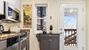A kitchen with stainless steel appliances, a granite countertop, a dark cabinet, and a door leading to a deck. - Outpost: Pitchfork 452 - Close to Snow King Mtn! (Jackson)