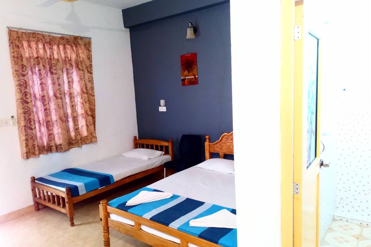 A room with two single beds, a ceiling fan, a wall-mounted light, and a door.