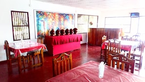 A dining area with wooden tables and chairs, a red tablecloth-covered table, and a colorful painting on the wall. - Nilaveli Hotel Onethra (Trincomalee)
