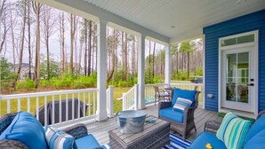 A covered porch with wicker furniture, a metal bucket, and a view of a forest. - Coastal Club * 6BR Luxury House (Lewes)