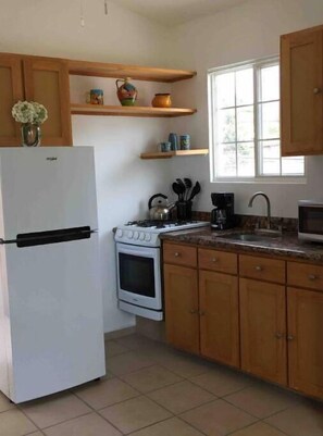 A kitchen with a refrigerator, stove, oven, wooden cabinets, and a window providing natural light.