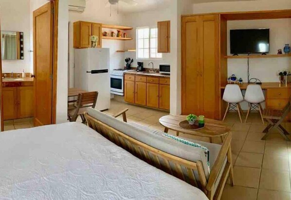 A room with a bed, a dining table, a kitchen area, and a TV.