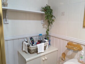 Un baño con tocador blanco, una planta y artículos de aseo sobre el mostrador.