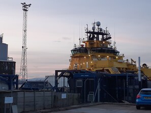 Un barco amarillo grande atracado en un puerto con una torre de control y diversos equipos.