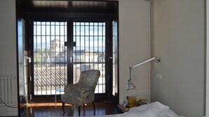 A bedroom with a bed, a chair, a desk, and a window with a view of buildings. - House with garden and views in a natural area 15' from the bustling city center (Granada)