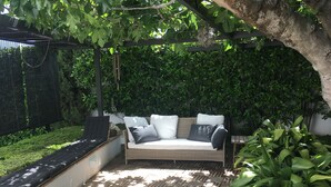 A covered outdoor seating area with a cushioned sofa, a patterned floor, and lush greenery. - House with garden and views in a natural area 15' from the bustling city center (Granada)