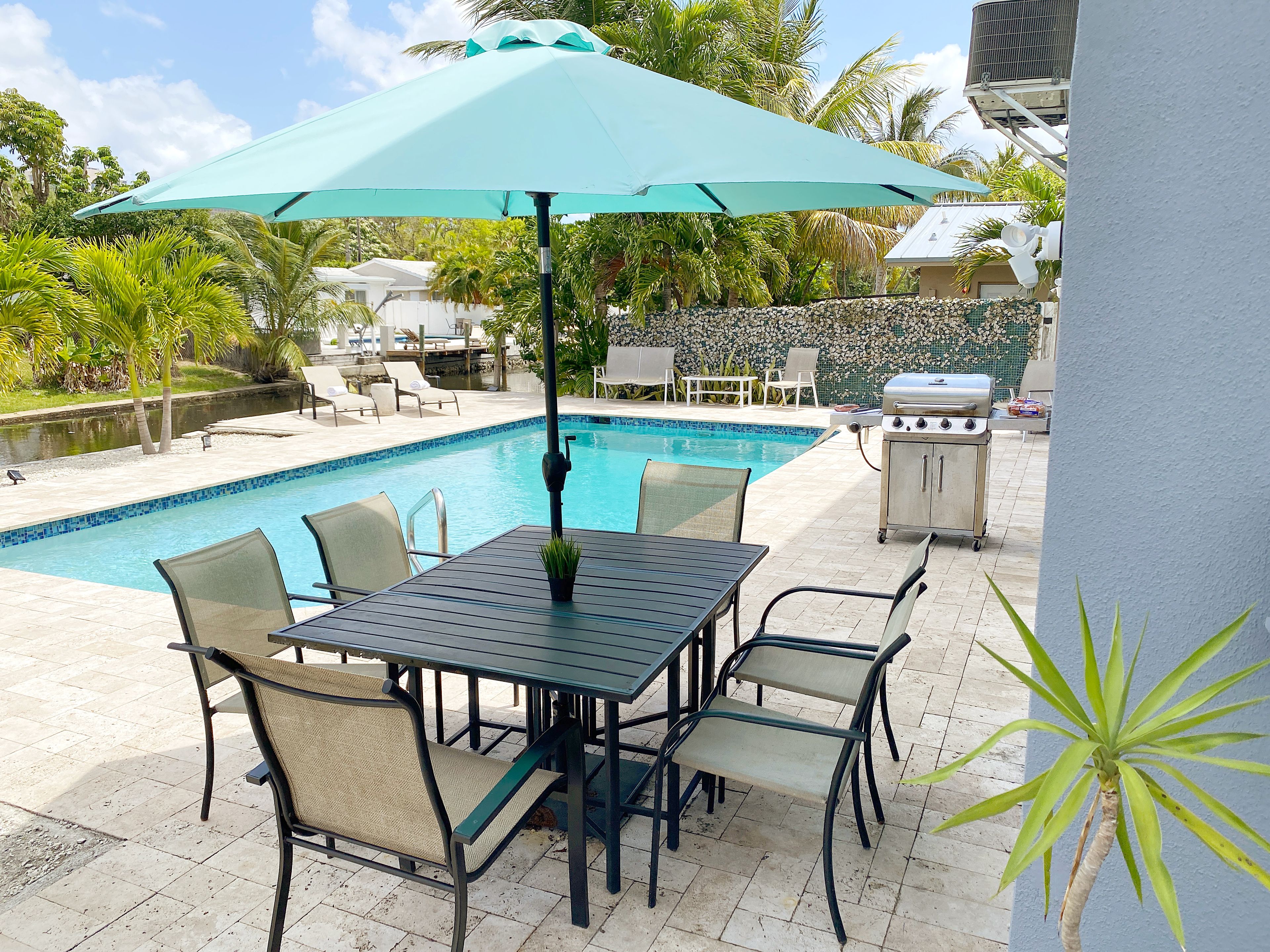 A poolside area with a table and chairs, a grill, and a view of the pool.