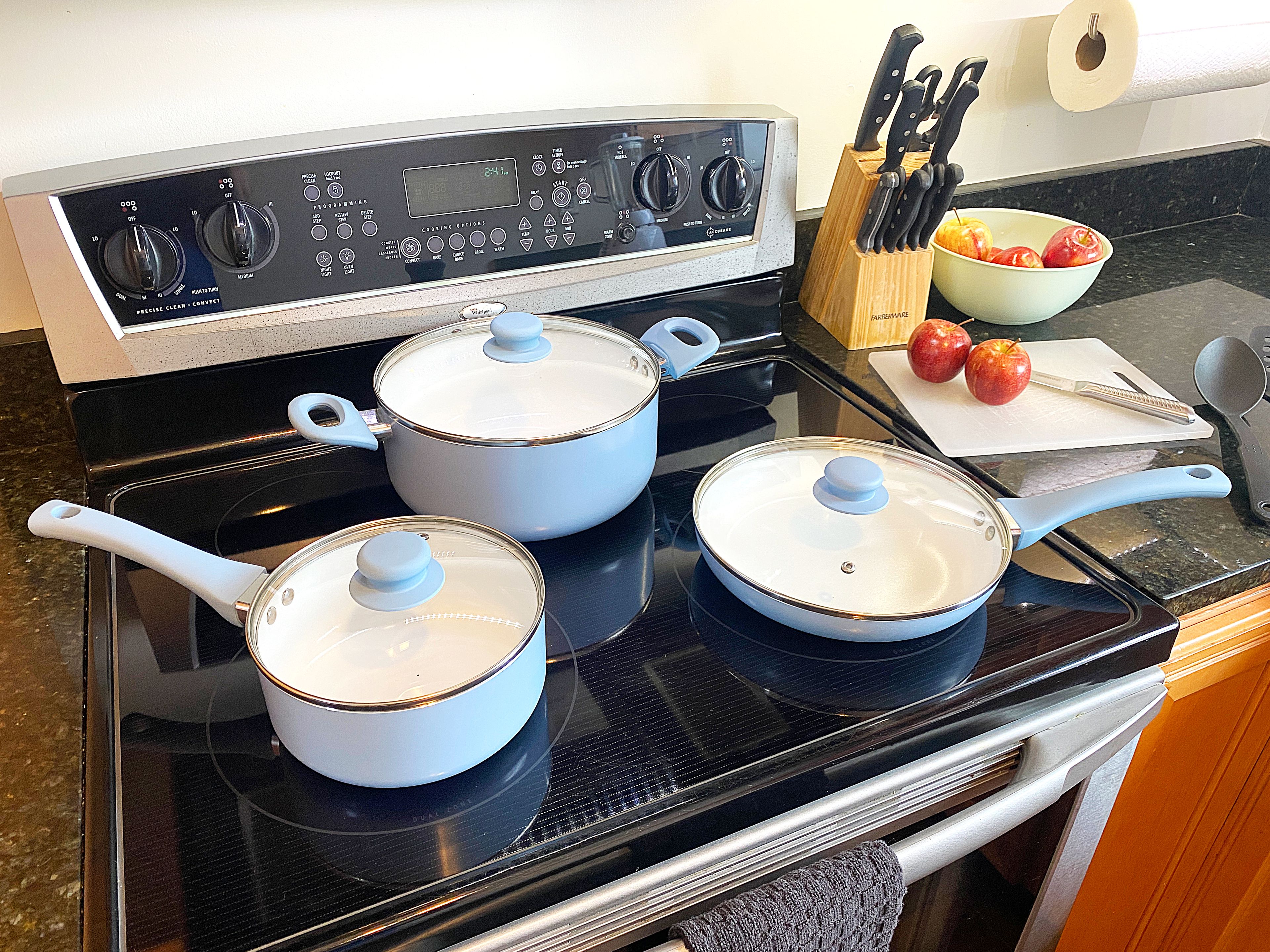 A kitchen with a stove, pots, a cutting board with apples, and a knife block.