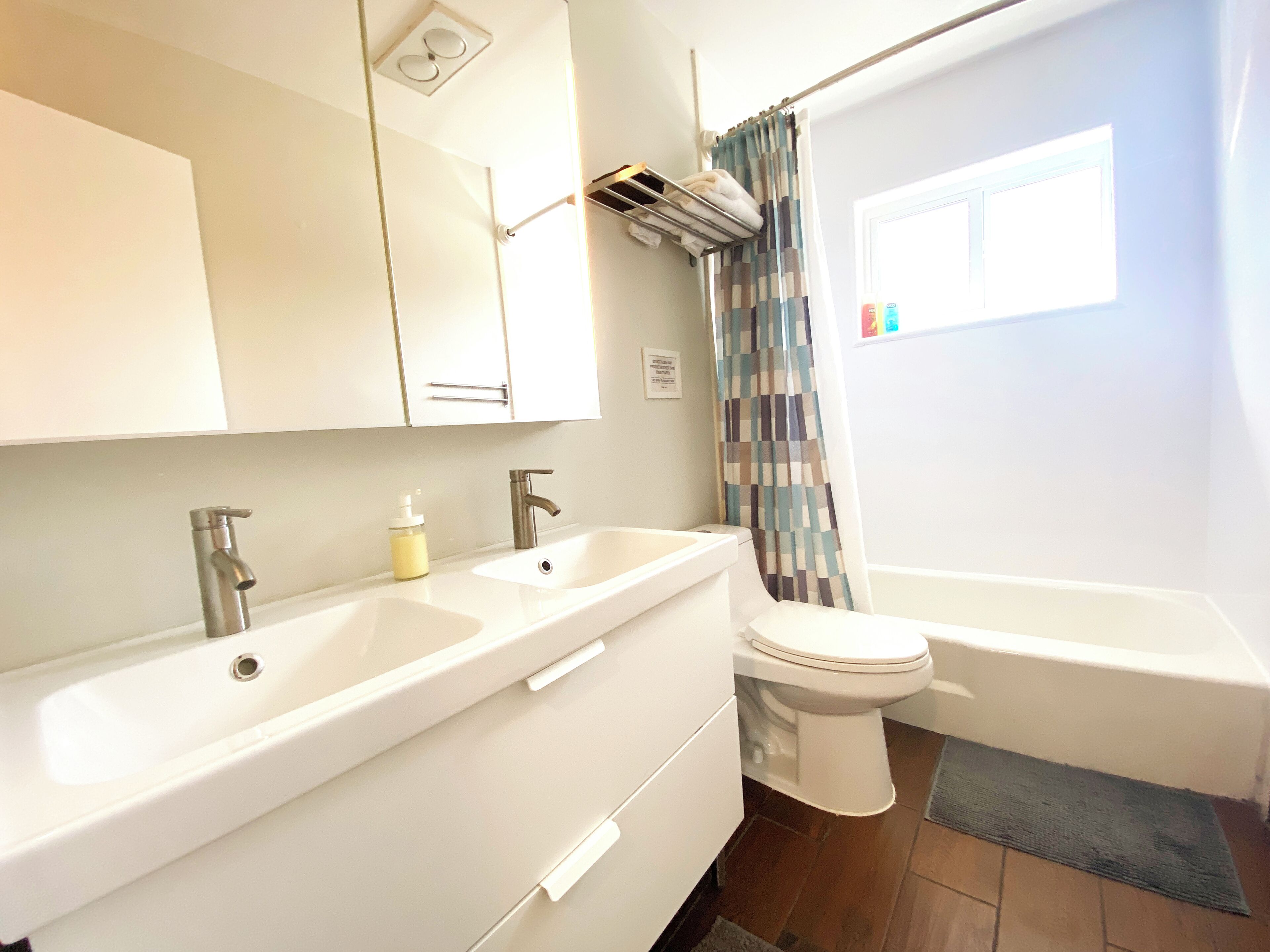 A bathroom with a white sink, two faucets, a toilet, and a bathtub. There is a shower curtain and a window with a view of the outside.