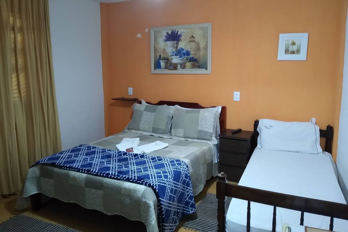 A bedroom with a bed, a nightstand, a bedside table, a ceiling fan, and a painting on the wall.