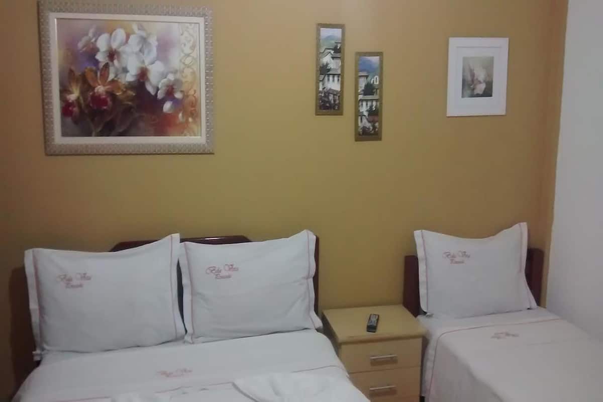A hotel room with two single beds, each with a pillow and a bedside table. There are three framed pictures on the wall.