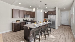 Une cuisine moderne avec des meubles en bois foncé, un plan de travail en granit, des appareils électroménagers en acier inoxydable et des luminaires suspendus.