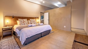 A modern bedroom with a large bed, wooden headboard, and a nightstand with a lamp.