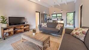 A modern living room with a flat-screen TV, grey sofas, and a kitchen in the background.