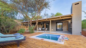 A modern outdoor pool area with wooden decking, lounge chairs, and a dining setup.