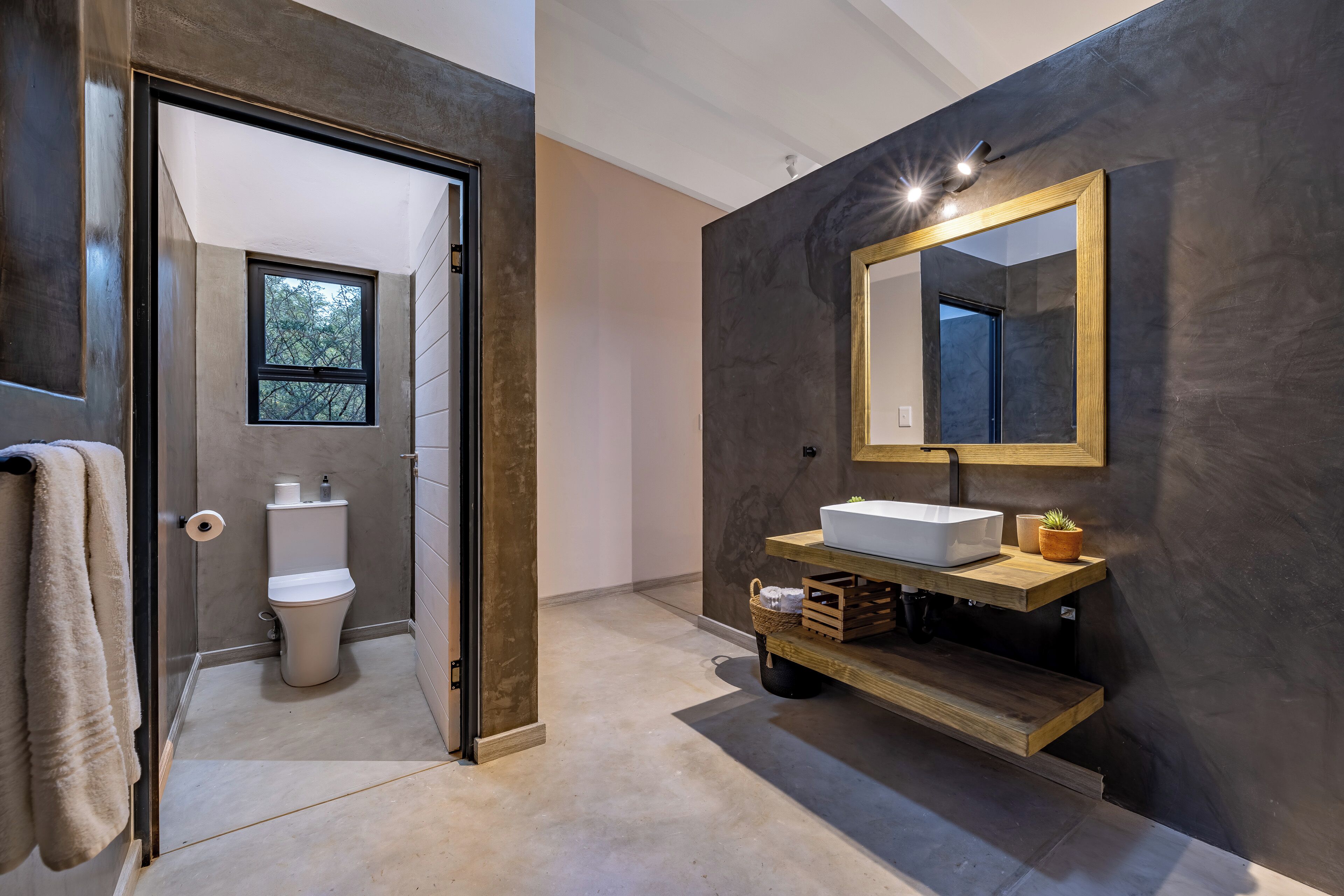 A modern bathroom with a large mirror, a white sink, and a wooden shelf.