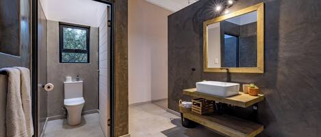 A modern bathroom with a large mirror, a white sink, and a wooden shelf.