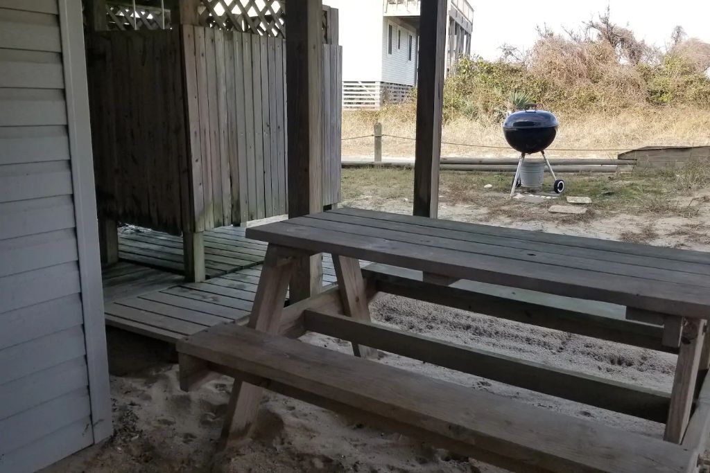 Een houten picknicktafel in een achtertuin, met een barbecuegrill op de achtergrond.