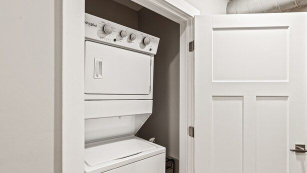 Un lavadero blanco con lavadora y secadora apiladas, una puerta y un tendedero de metal.