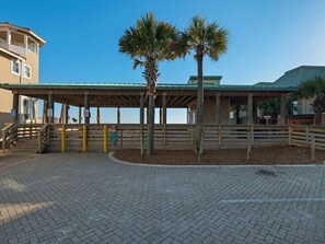 A covered outdoor area with a wooden fence, palm trees, and a building with a green roof.