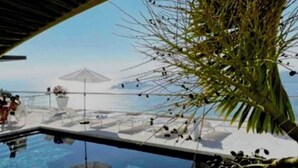 Un'area piscina lussuosa con acqua cristallina, un solarium in legno e vista sull'oceano.