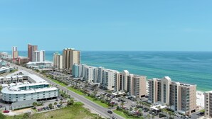 Un hotel frente al mar con varios edificios altos, un estacionamiento y vista al océano.