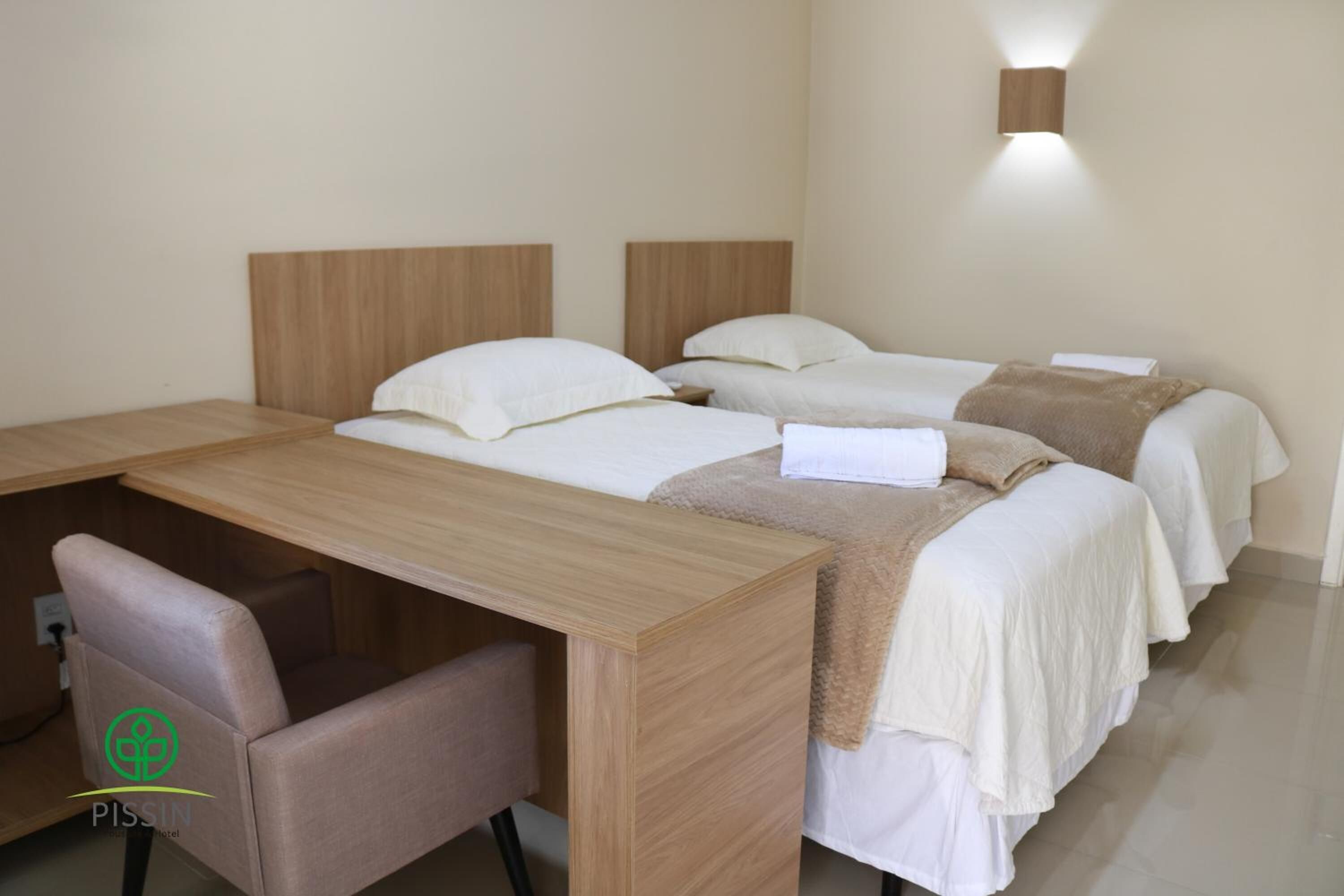 A hotel room with three beds, a wooden desk, and a chair.