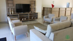 Een moderne woonkamer met een flatscreen televisie, inbouwplanken en een zithoek met banken en fauteuils.