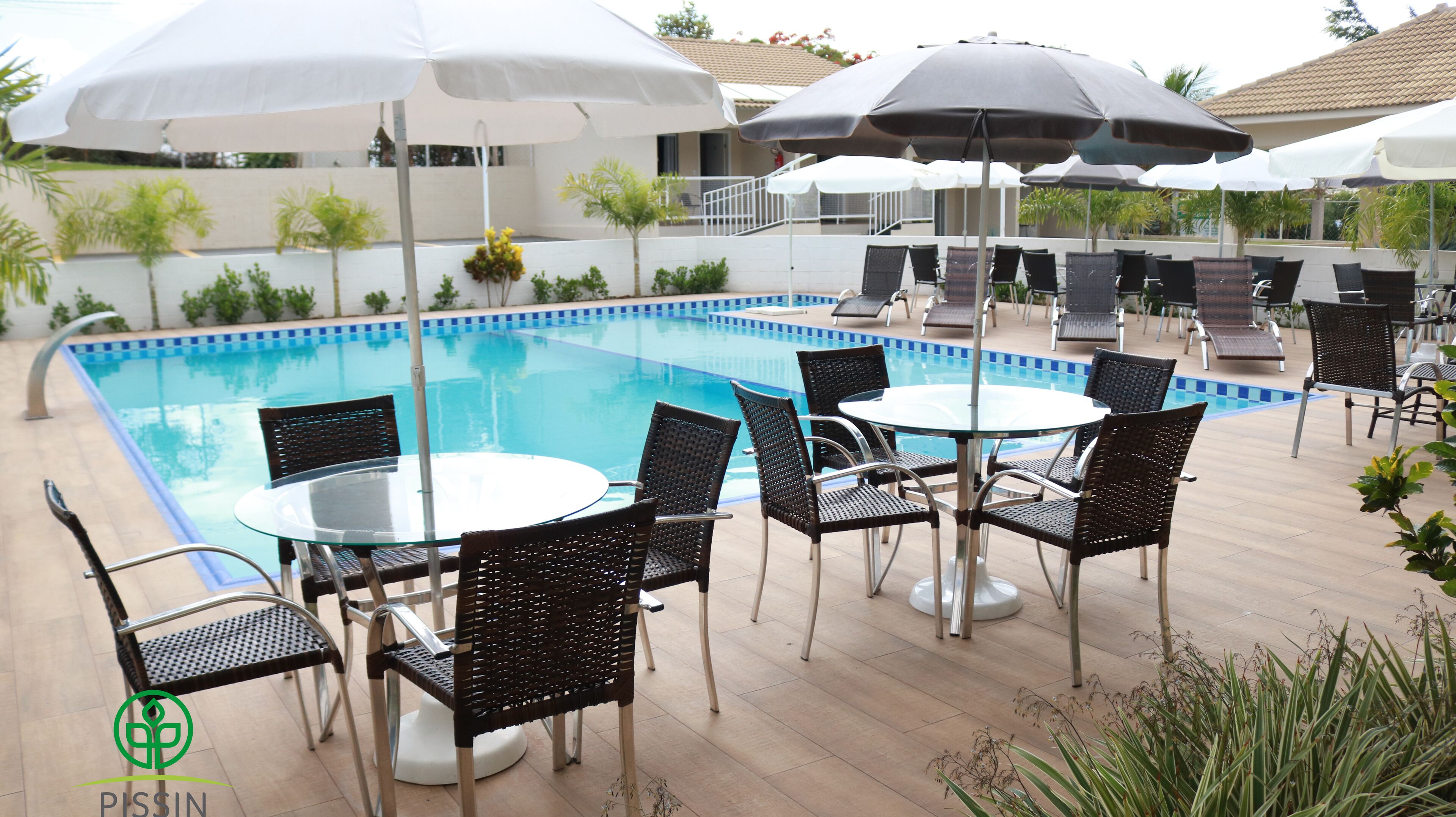 Zona de piscina con sillas reclinables y sombrillas, una piscina azul cristalina y una terraza con baldosas.